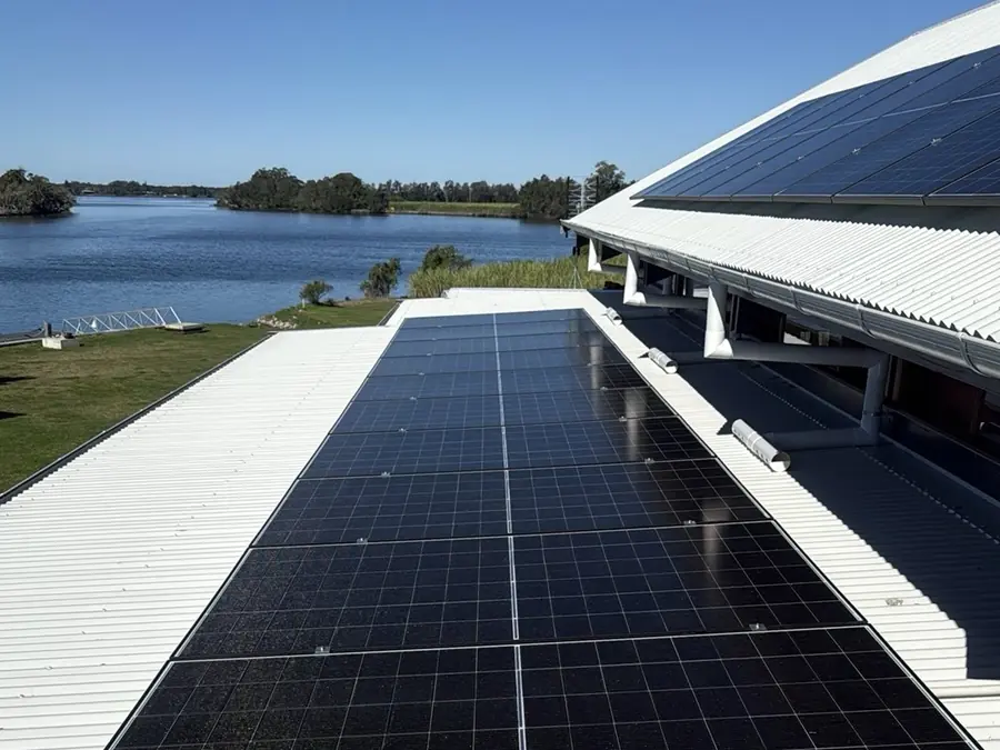 Rooftop solar panels installed on a metal roof beside a waterway