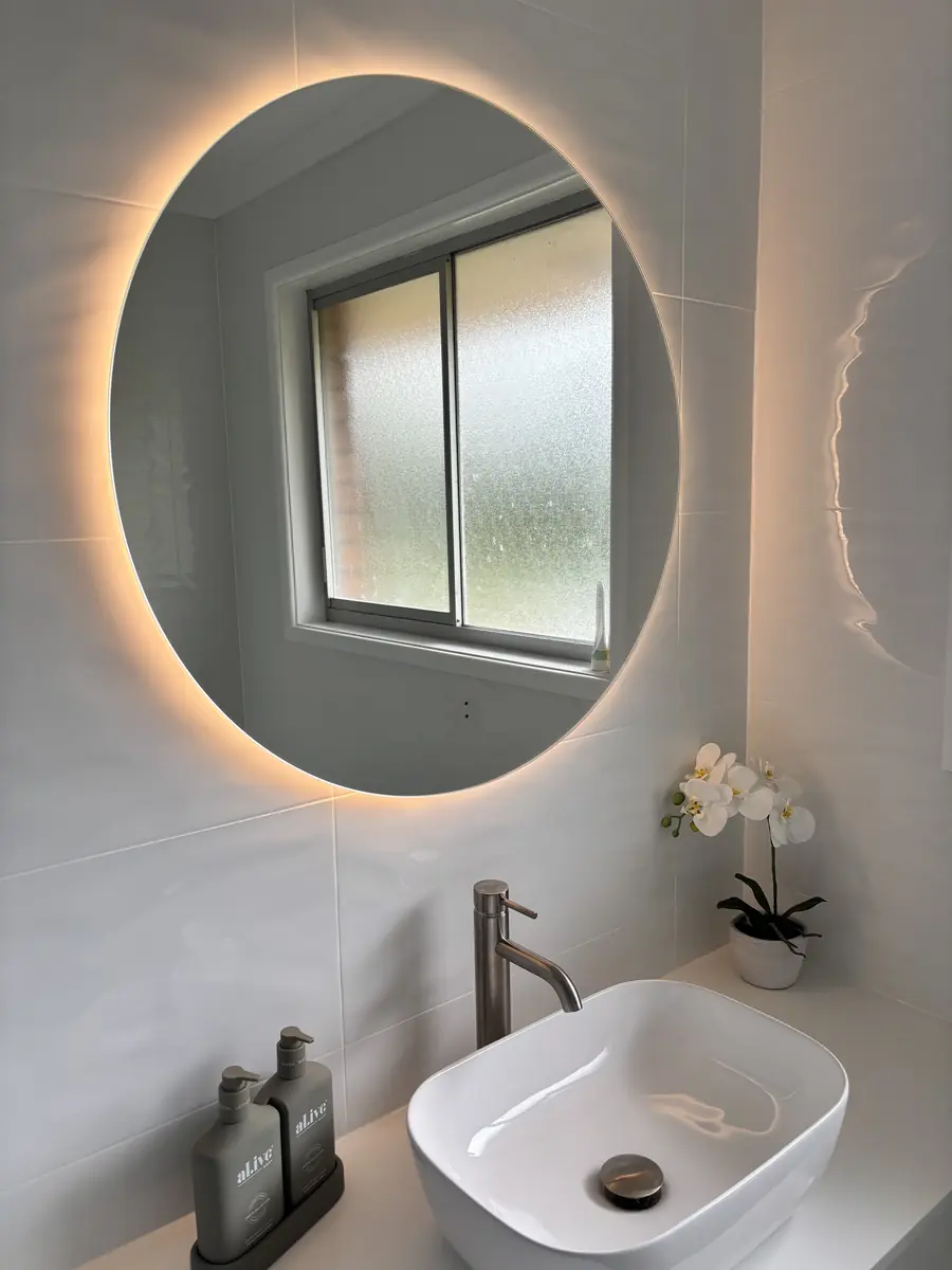 Illuminated circular mirror above a bathroom vanity with a white basin