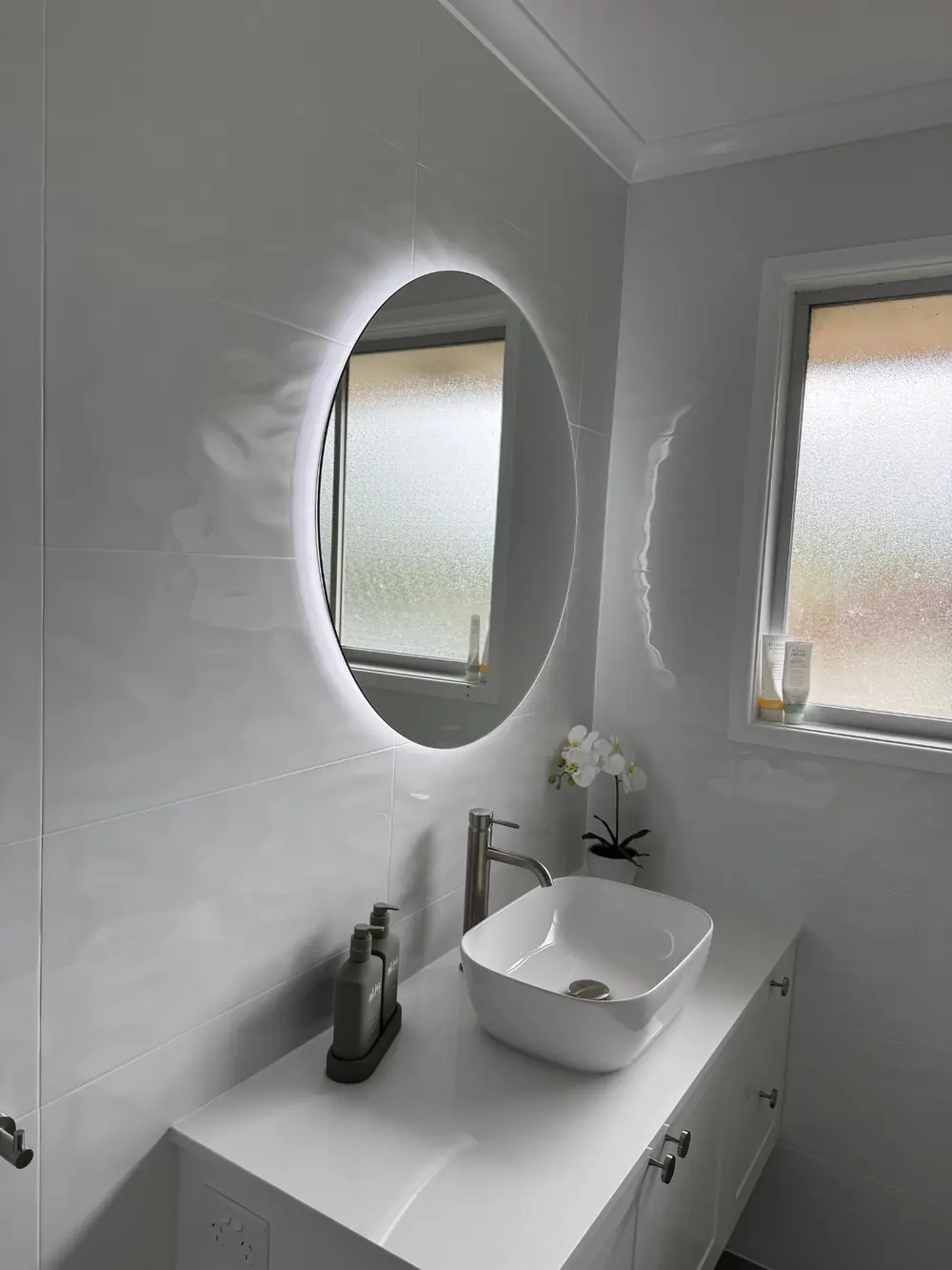 Illuminated oval mirror above a bathroom vanity with a white basin