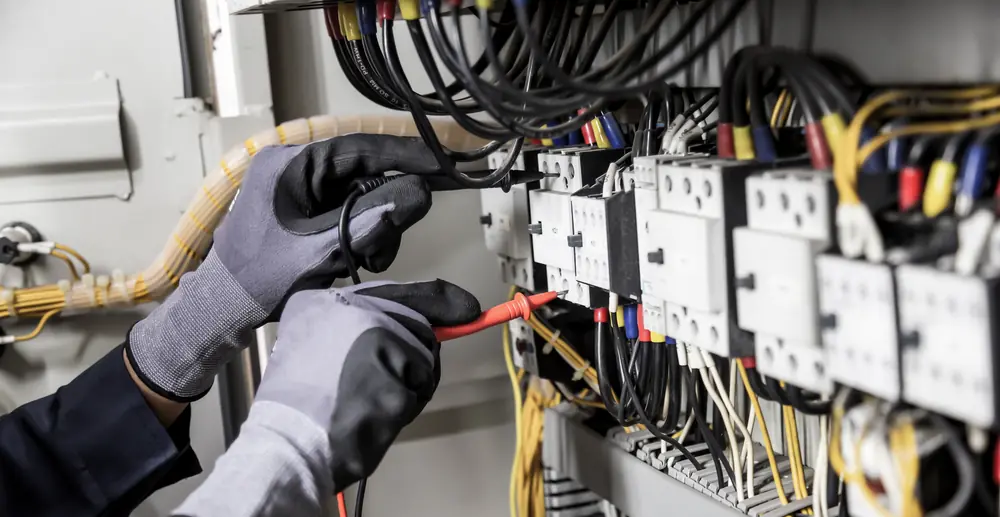 Electrician's gloved hands checking components inside a commercial electrical control panel