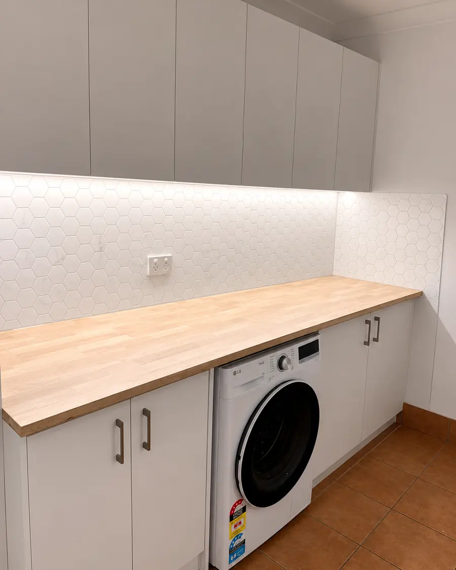 Under-cabinet lighting above a timber laundry bench and washing machine