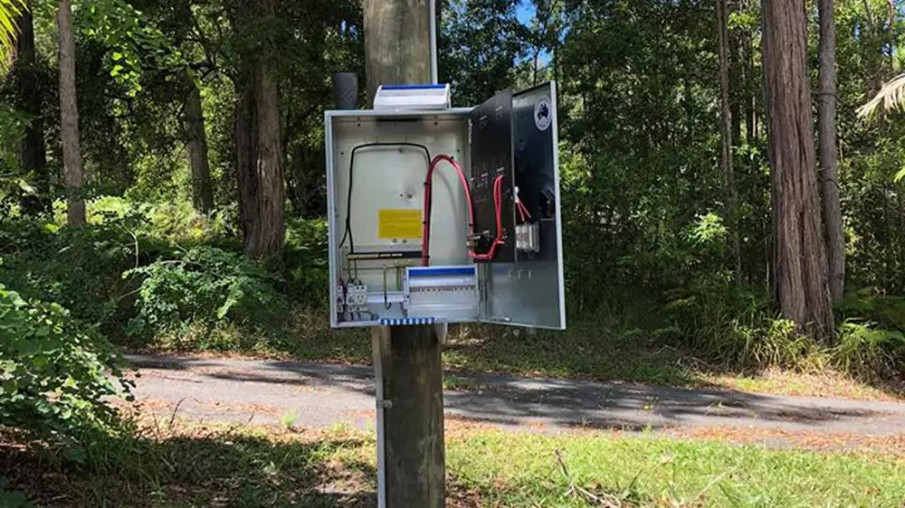 Open electrical service enclosure mounted on a post beside a rural driveway