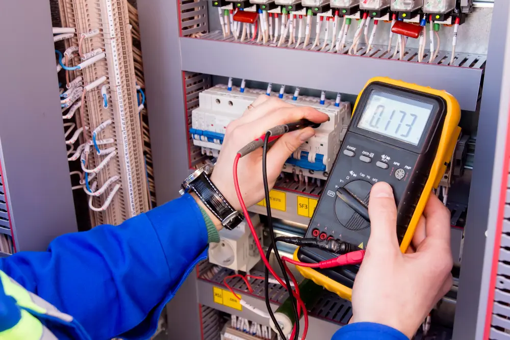 Electrician testing circuit breakers inside an electrical switchboard with a multimeter