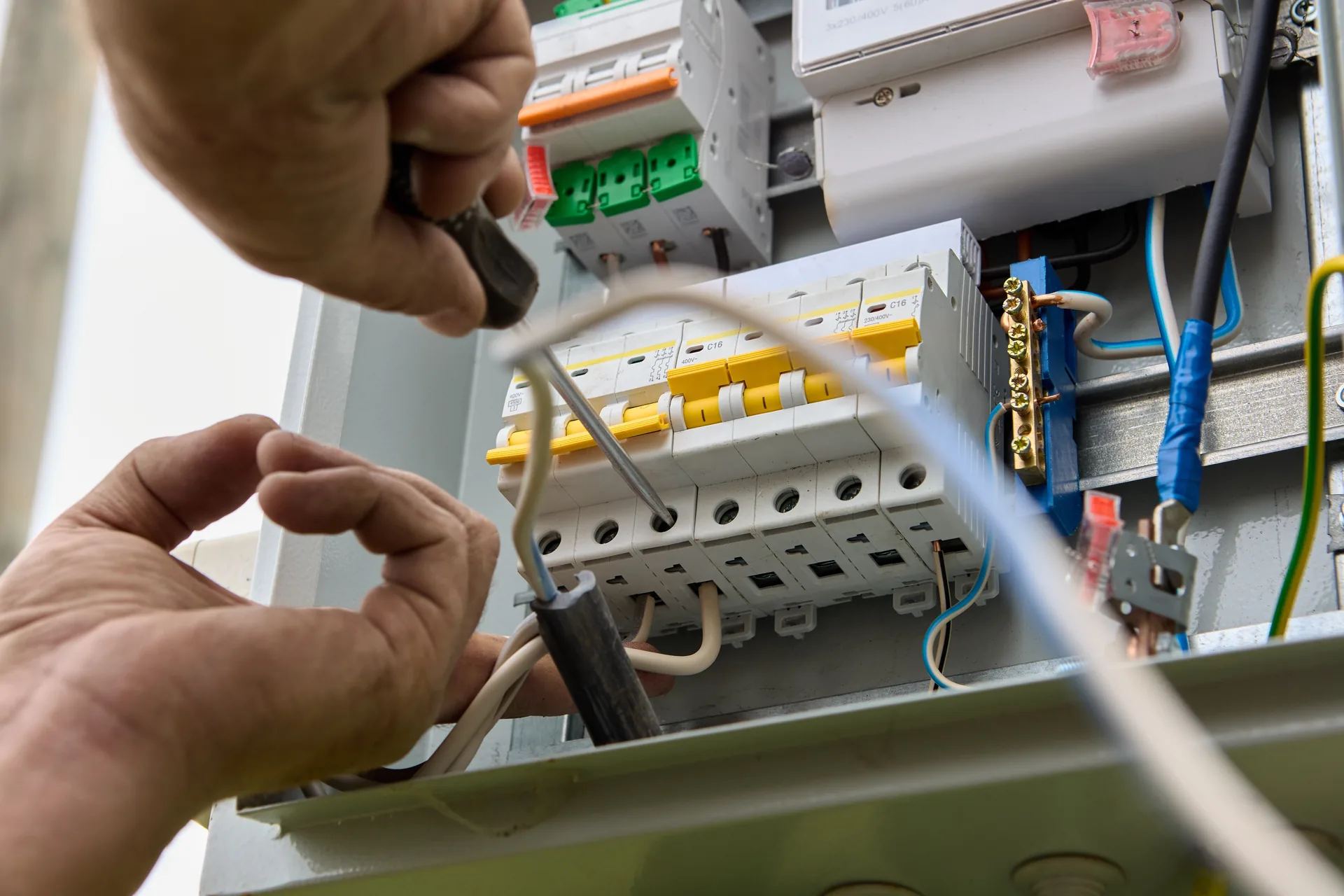 Hands working inside an open electrical switchboard with circuit breakers and wiring
